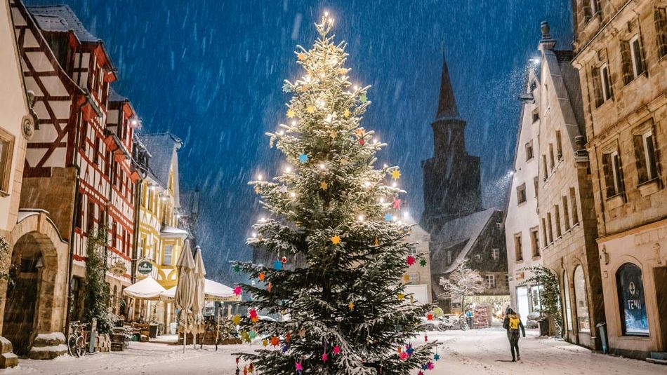 Geschmückter Weihnachtsbaum am Grünen Markt bei abendlichem Schneefall. Im Hintergrund der Kirchturm von Sankt Michael.