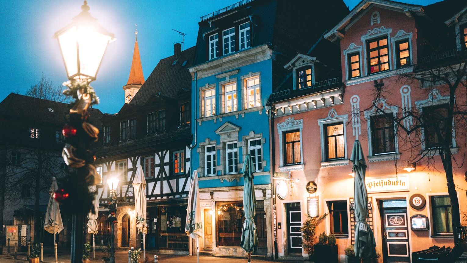 Häuserzeile in der weihnachtlich dekorierten Gustavstraße am Abend. Im Hintergrund der beleuchtete Kirchturm von Sankt Michael.